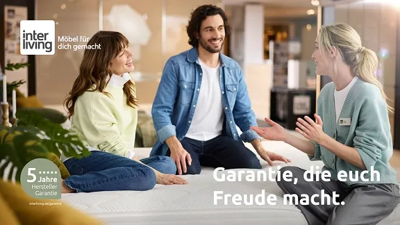 Ein Paar sitzt auf einem Bett und unterhält sich mit einem Verkäufer in einem Interliving-Möbelhaus. Dabei wird auf die 5-jährige Garantie hingewiesen.